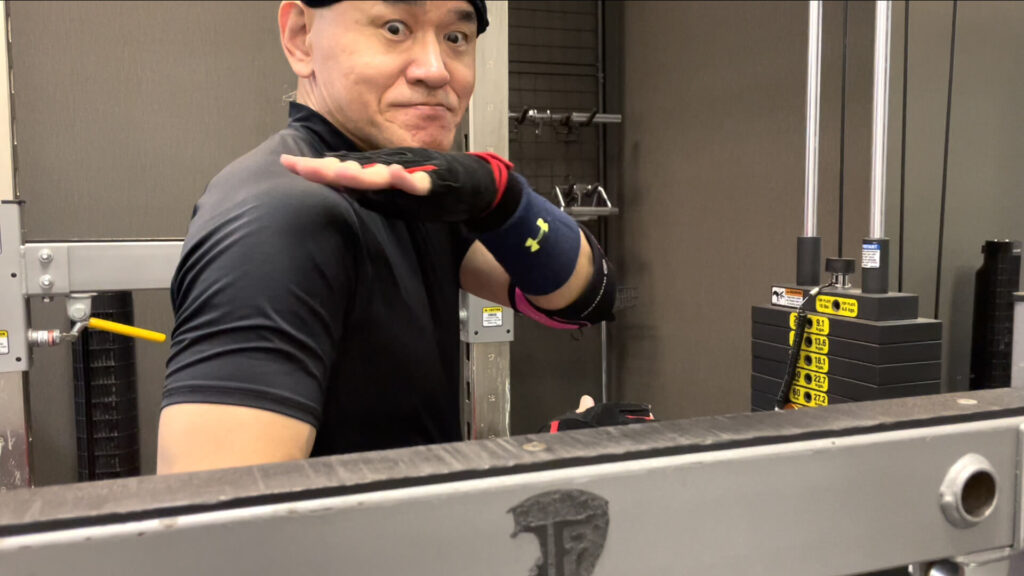 長崎県南島原市で人気殺到の健康体操教室ZUTTOWAKAIの代表トレーナー太田祥平がスクワットのやり方を見せている様子。セーフティーバーの高さを調整するため僧帽筋の高さを確認している