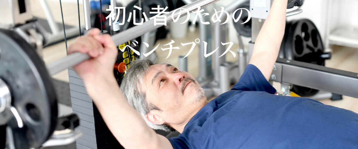 「初心者のためのベンチプレス」という白い文字。その背後には、ベンチプレスを行う白髪の男性。青い半袖Tシャツを着ている。