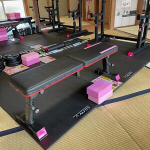 ZUTTOWAKAI 南島原加津佐のトレーニングスペース。畳敷きの和室にゴムマットを敷き、ベンチプレス台やスクワットラック、プレートやバーベルなどの本格的な筋トレ器具が整然と配置されている。明るい自然光が差し込む和モダンな空間。
