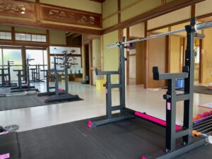 南島原市南有馬のZUTTOWAKAIトレーニングジム内観。畳と木の温もりを活かした和の空間に、ピンクのアクセントが映えるバーベルラックが整然と並ぶ。高齢者も安心して筋力トレーニングができる、安全設計の設備が特徴。