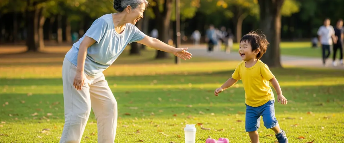 晴れた日に公園の芝生の上で、白髪が交じる女性が孫の男の子と楽しそうに鬼ごっこをしています。足元にはトレーニング用のダンベルとプロテインシェイカーが置かれています。