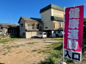 太良町にあるフィットネスジムであるZUTTOWAKAIの外観。大きな「健康運動入口」の赤い旗が目印。建物横には銀色の軽バンが停まっています。